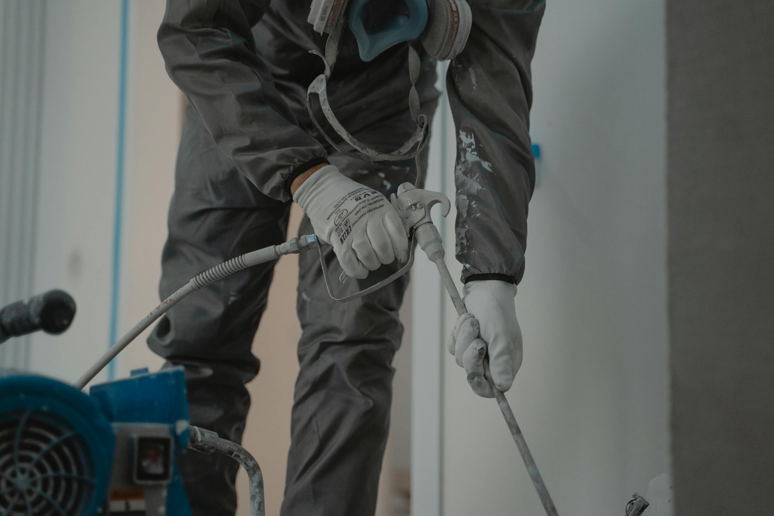 Worker in protective gear using a power spray for indoor renovation.